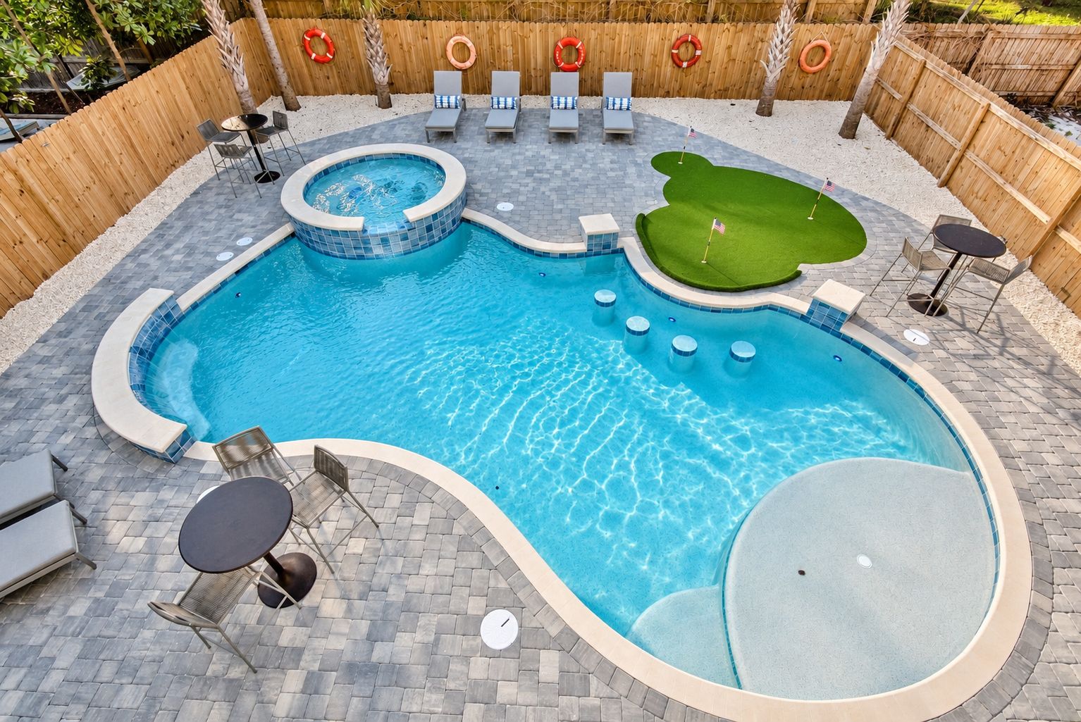 A swimming pool with a hot tub, lounge chairs, and a small green area.