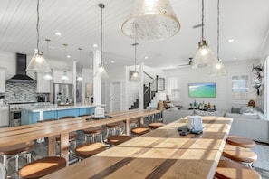Et moderne køkken med en central ø, hængende lamper og et spiseområde med barstole.