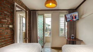 A hotel room with two beds, a television, a small table with bottles, a brick wall, a balcony door, and a tiled floor. - Hanoi Rendezvous Hostel (Hanoi)
