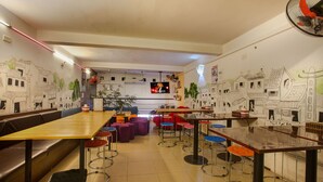 A restaurant with high tables and stools, a TV screen, and walls decorated with drawings. - Hanoi Rendezvous Hostel (Hanoi)