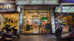 The exterior of the Rendezvous Hanoi Hostel, featuring a tour booking office, a sign for a motorbike rental service, and a nearby shop named "Colin's Cafe". - Hanoi Rendezvous Hostel (Hanoi)