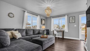 A modern living room with a grey sectional sofa, a chandelier, and a desk with a chair. - Barnegat Bay Cottage: A 'MyShoreCottage' Property (South Seaside Park)