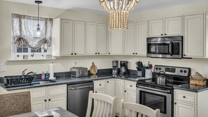 A kitchen with white cabinets, a stainless steel microwave, a stove, and a chandelier. - Barnegat Bay Cottage: A 'MyShoreCottage' Property (South Seaside Park)