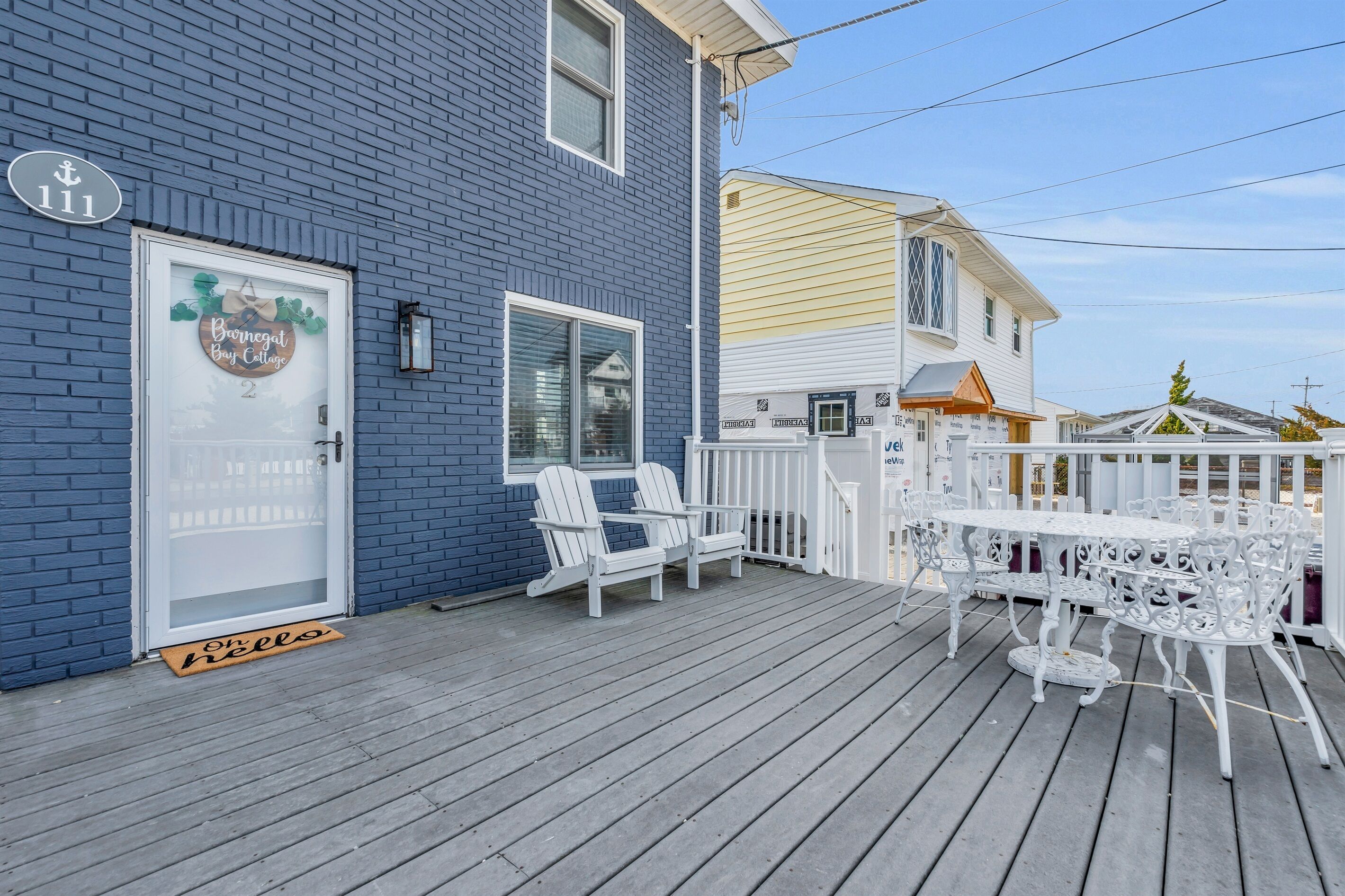 A blue building with a white door, a porch with white chairs and a table, and a white fence.
