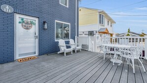A blue building with a white door, a porch with white chairs and a table, and a white fence. - Barnegat Bay Cottage: A 'MyShoreCottage' Property (South Seaside Park)