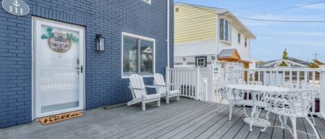 A blue building with a white door, a porch with white chairs and a table, and a white fence.