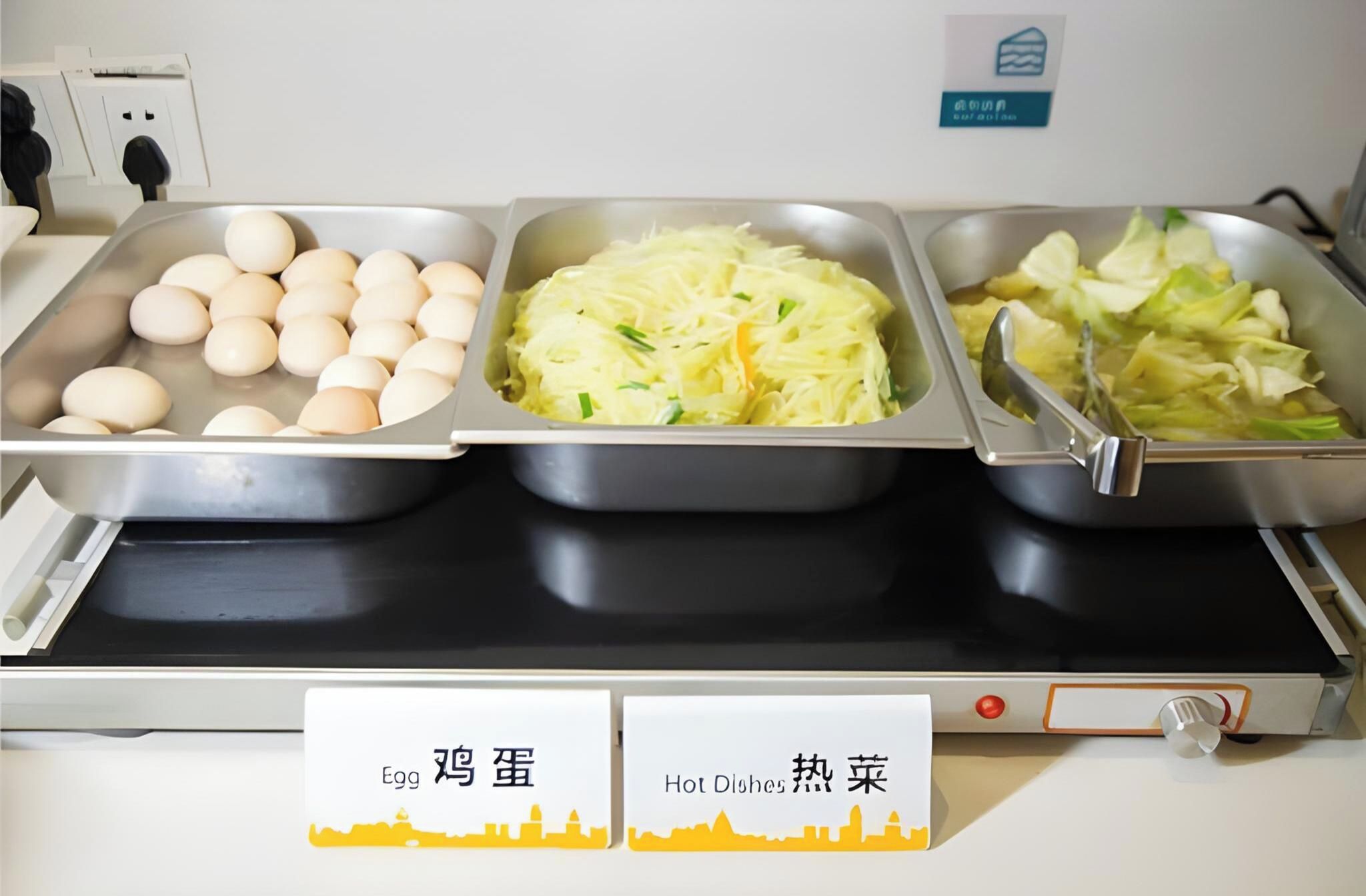 Un buffet proposant une variété de plats, chacun étant clairement identifié, notamment des œufs, des plats chauds et des légumes.
