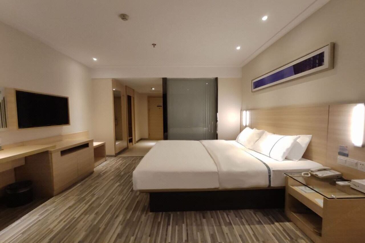 Ein Hotelzimmer mit einem großen Bett, einem Schreibtisch, einem Fernseher und einem Nachttisch mit Telefon.