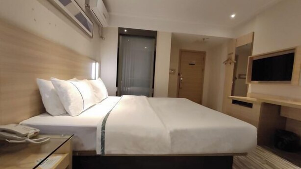 A hotel room with a large bed, a bedside telephone, a TV mounted on the wall, and a door leading to another room. - City Comfort Inn (Jingdezhen Xinchang Road Taoxichuan) (Jingdezhen)