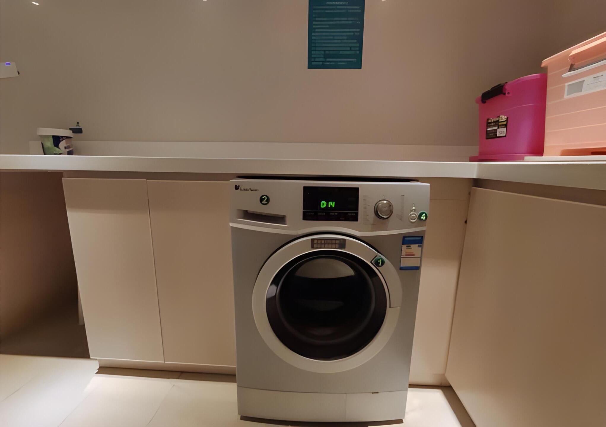 A compact, modern laundry room with a front-loading washing machine, a control panel, and a small shelf with storage bins.