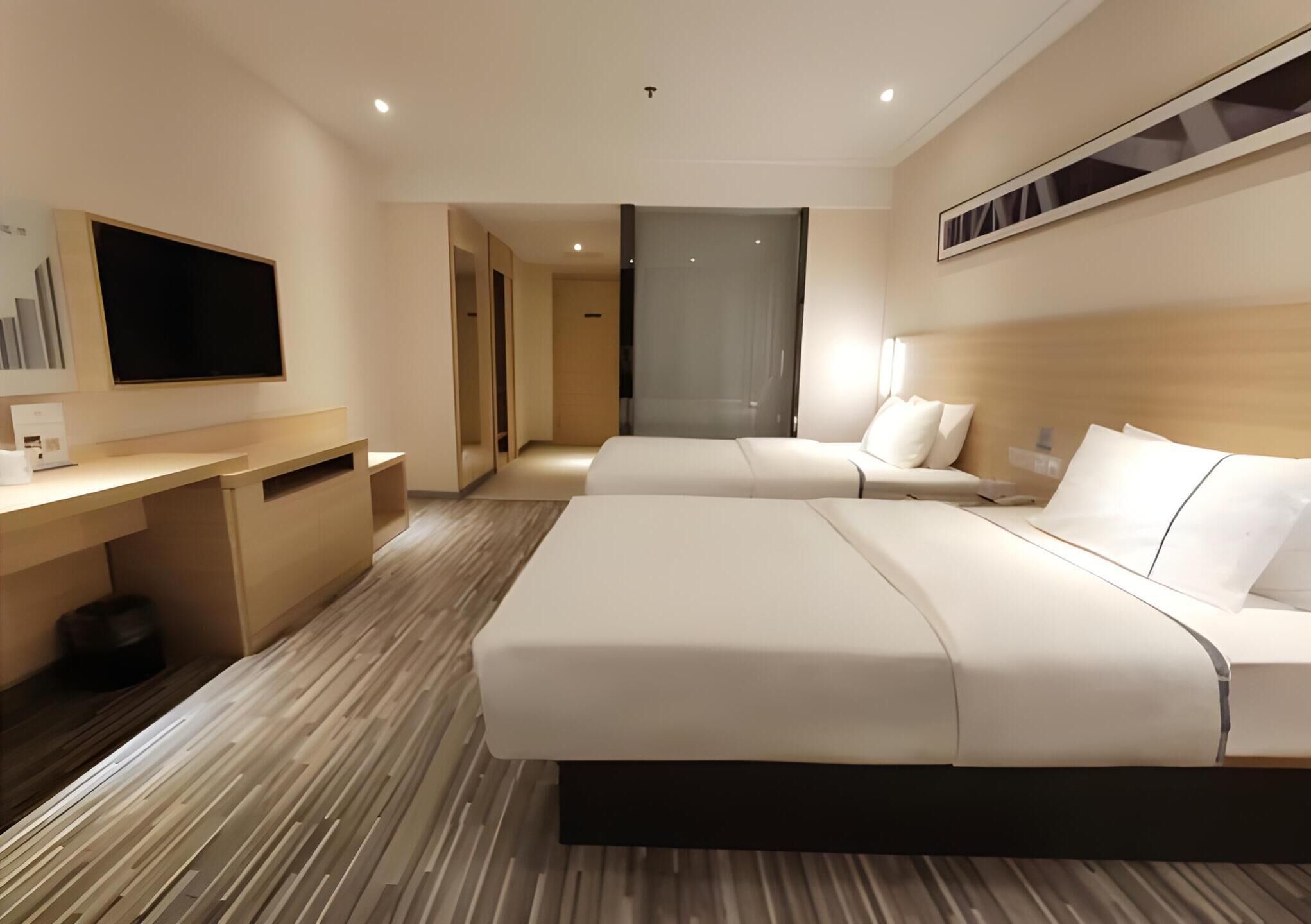 A hotel room with a large bed, a desk, a flat-screen TV, and a shower area.