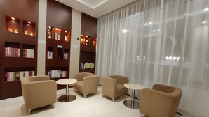 A modern lobby with beige sofas, small round tables, and bookshelves with books. - City Comfort Inn (Jingdezhen Xinchang Road Taoxichuan) (Jingdezhen)