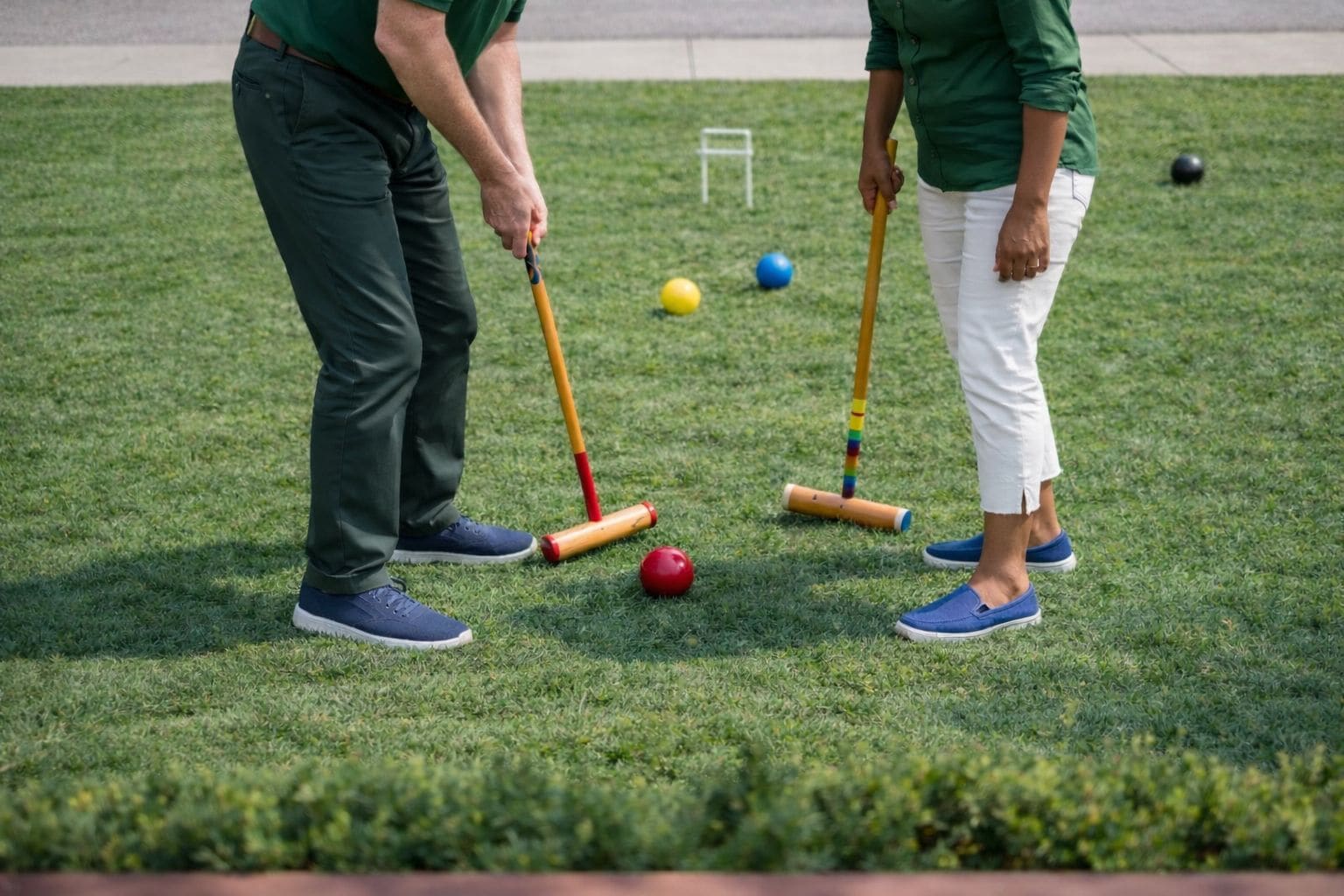 Two people playing croquet on a well-maintained lawn with a small white structure in the background.