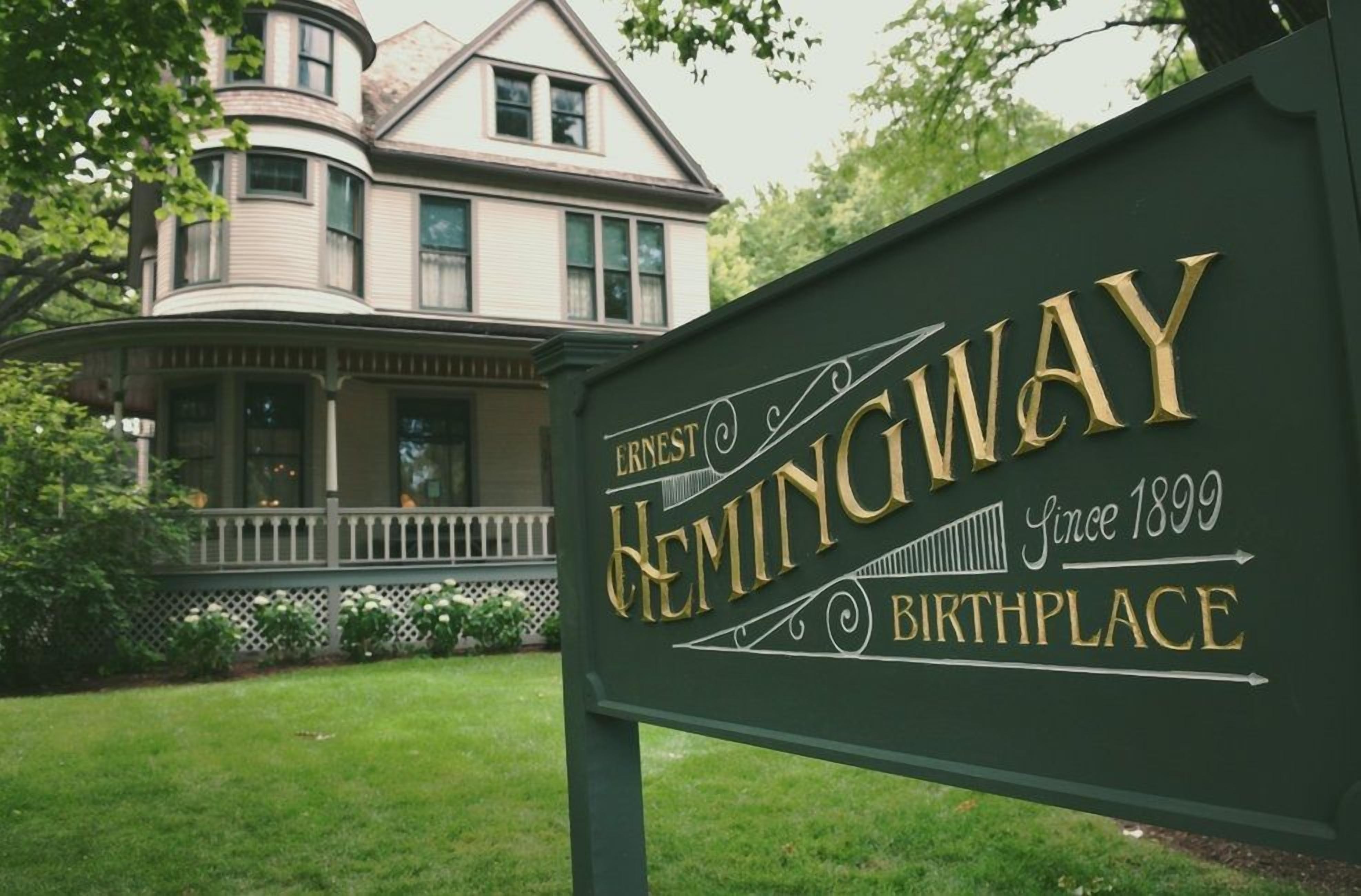 A sign for Hemingway Birthplace with a house in the background.