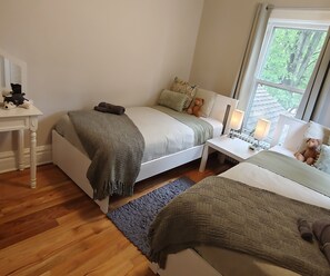 Quarto com cama, mesa de cabeceira, luminária e vista para o verde lá fora.