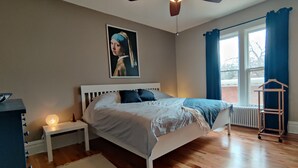 Een slaapkamer met een bed, een nachtkastje, een verwarming, een raam met gordijnen en een plafondventilator.