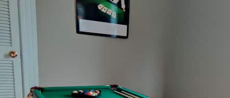 A pool table with balls and cues, a door with a golden doorknob, and a poster on the wall.