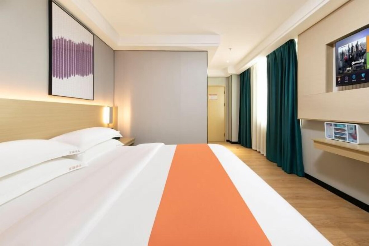 A hotel room with a bed, a flat-screen TV, a bedside table, and a wall-mounted artwork.