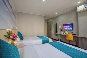 Une chambre d’hôtel avec deux lits, un bureau avec un ordinateur, une chaise et un téléviseur fixé au mur.