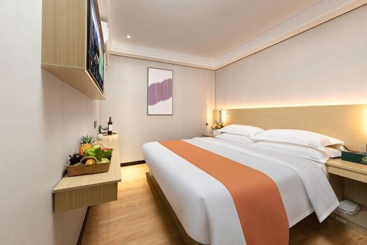 A hotel room with a bed, bedside table, wall art, and a small plant on the nightstand.