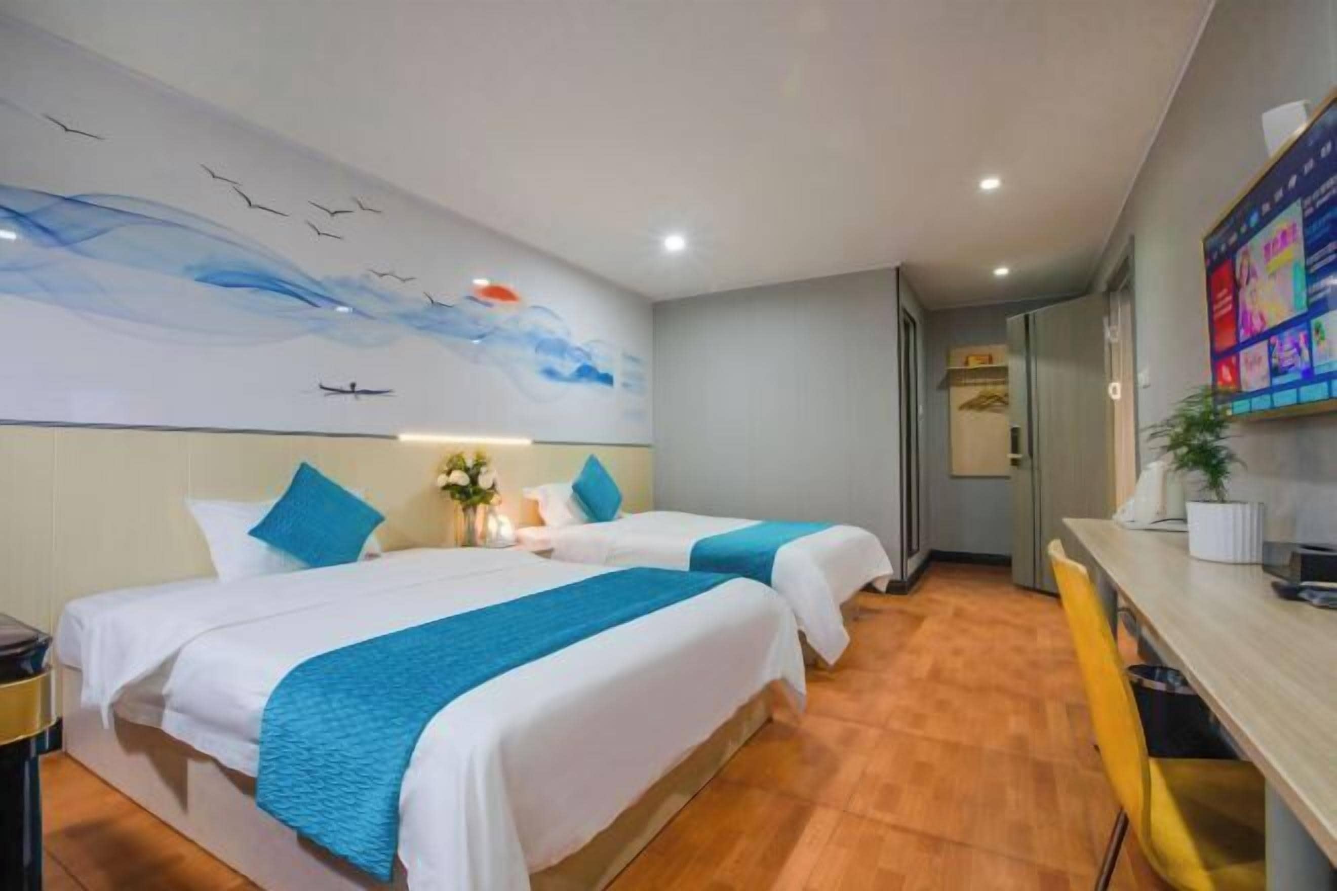 A hotel room with two beds, a wooden floor, a wall mural, a desk, and a chair.