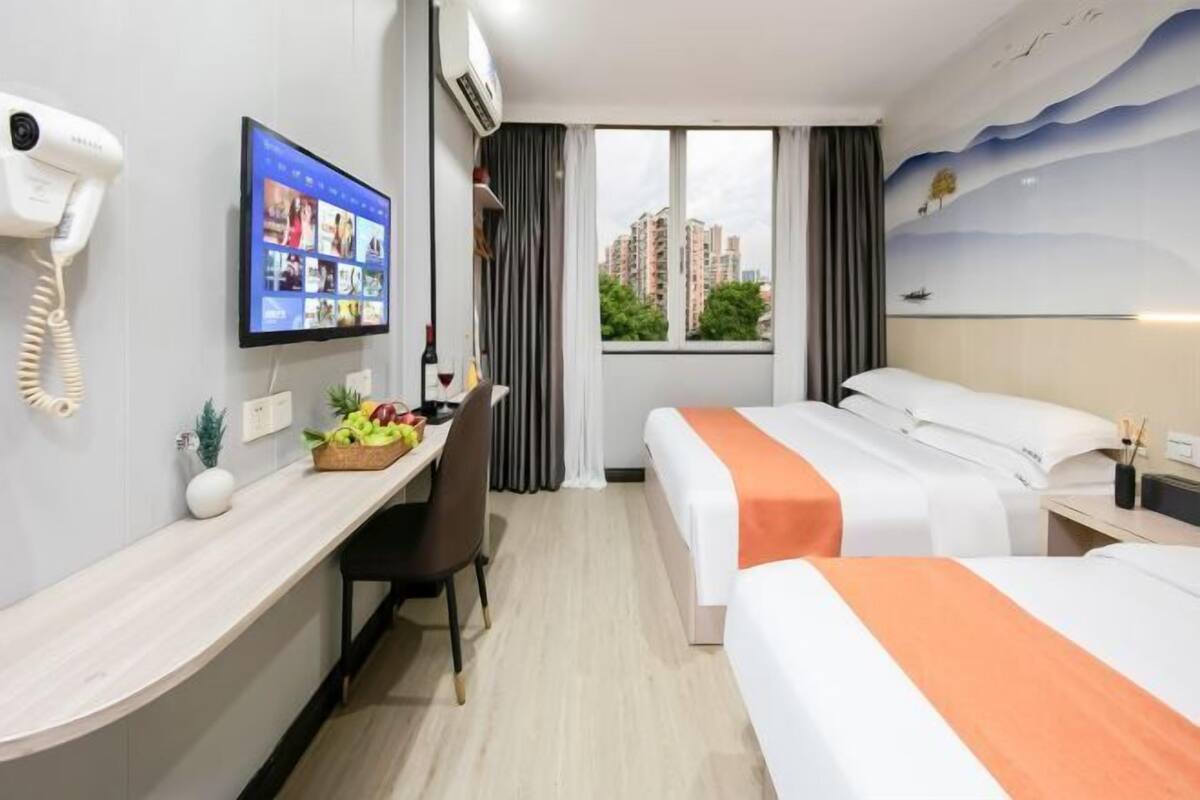A hotel room with a desk, two beds, a TV, and a view of buildings.