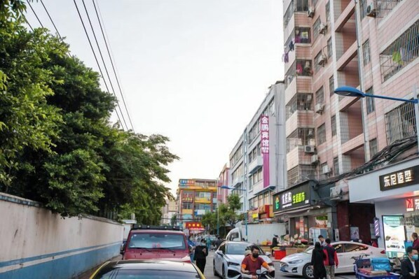 Une rue animée en milieu urbain, bordée d’immeubles à plusieurs étages, de boutiques et de voitures garées.