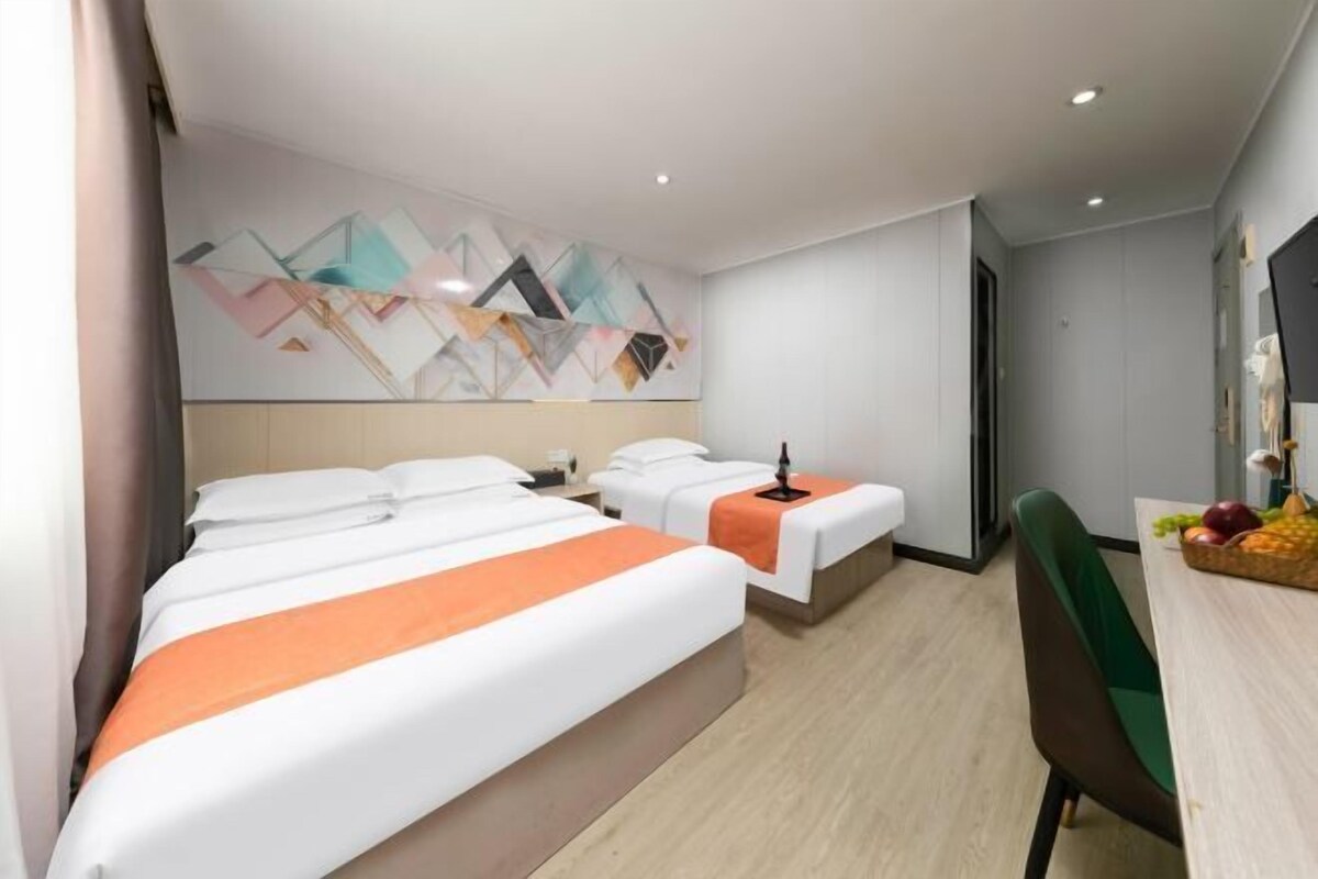 A hotel room with two beds, a desk, a chair, and a wall with geometric artwork.