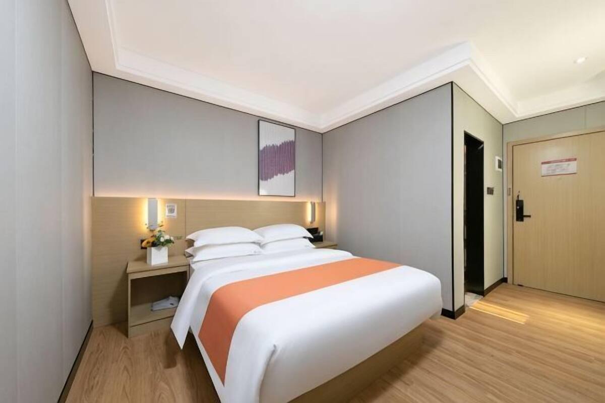 A hotel room with a bed, bedside table, lamp, and a door.