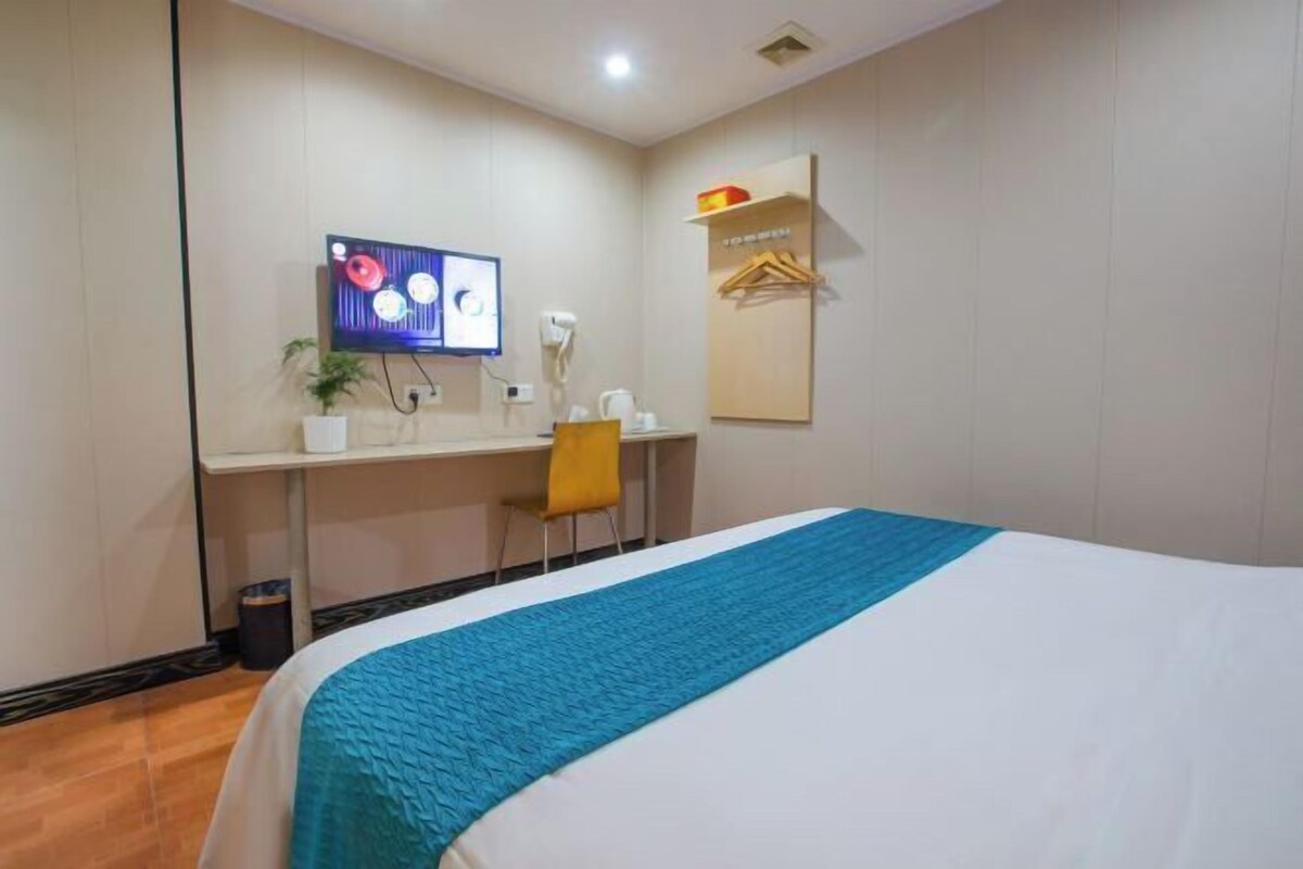 Une chambre d’hôtel avec un lit, un bureau avec un ordinateur, une chaise, une télévision et une petite plante.