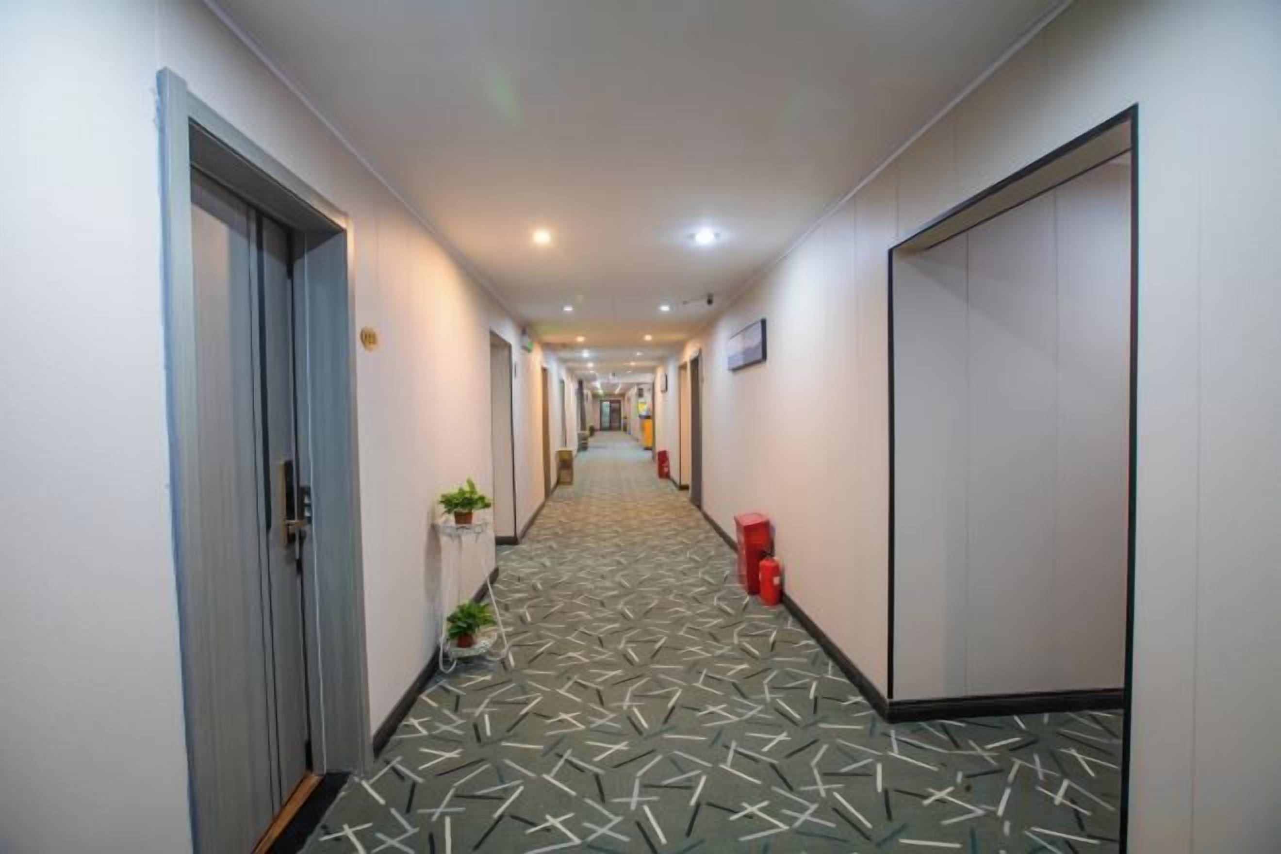 A hotel hallway with a patterned floor, doors, and a trash bin.