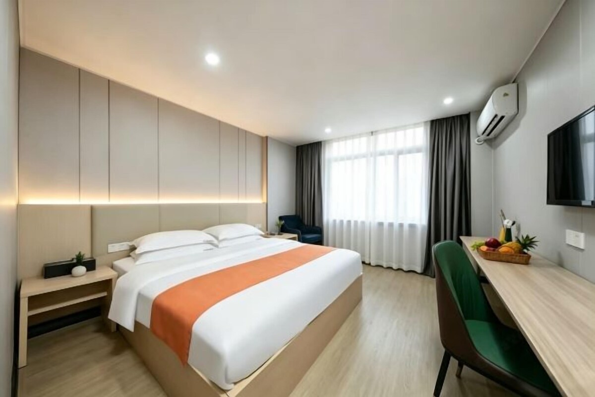 A modern hotel room with a bed, bedside table, desk, and chair.