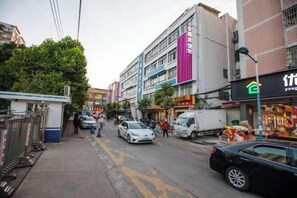 Une vue de rue avec des immeubles, une voiture blanche et une voiture noire garées sur le bord.