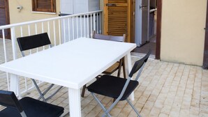 Ein weißer Tisch mit vier schwarzen Stühlen auf einer gefliesten Terrasse.