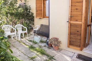 Une terrasse avec deux chaises en plastique blanc, un banc en bois et une plante en pot.