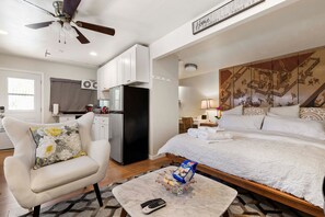 Une chambre d’hôtel équipée d’un lit, d’un bureau, d’une chaise, d’un ventilateur de plafond et d’un coin cuisine.