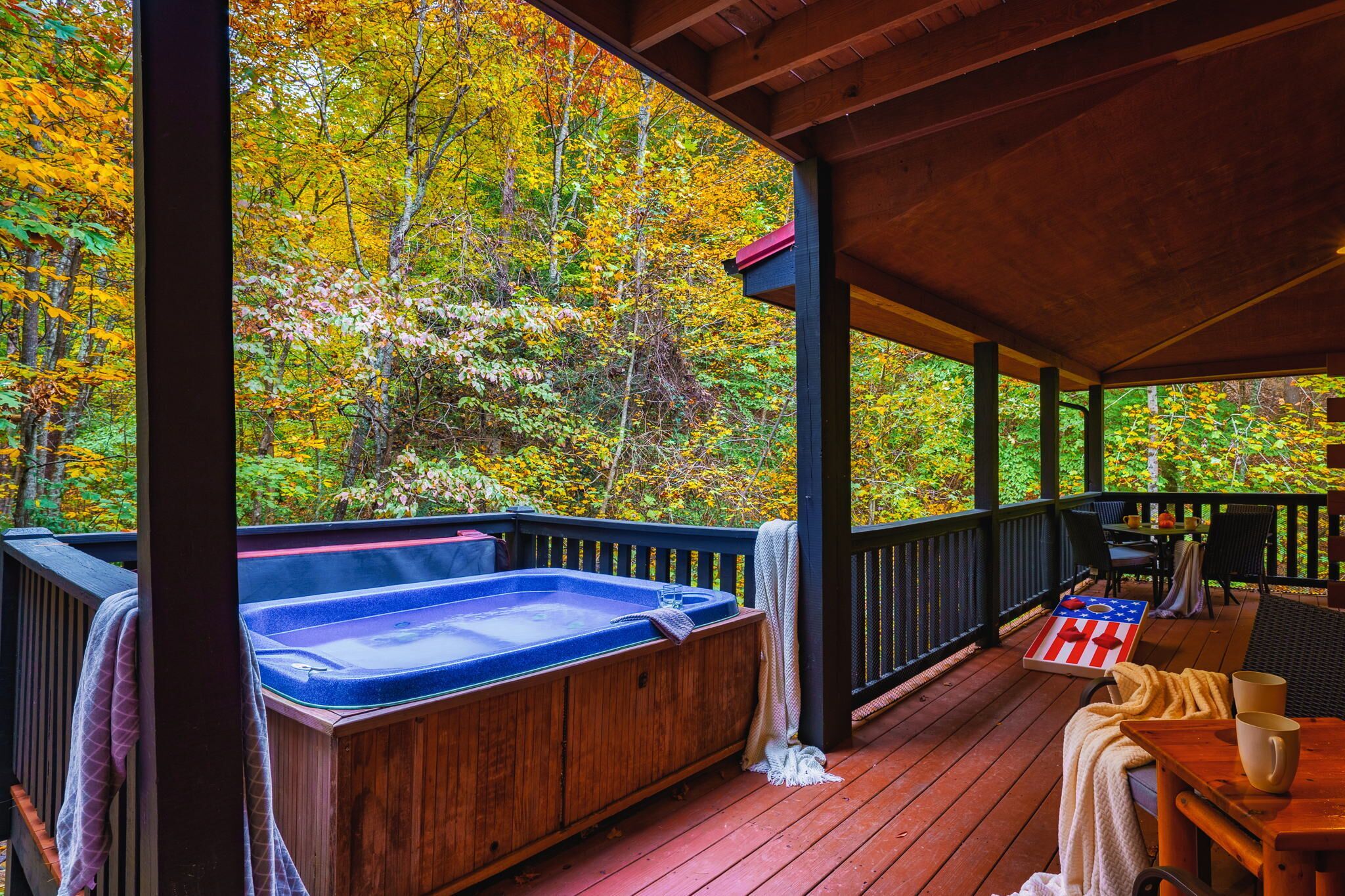 Eine Holzterrasse mit Whirlpool, Sitzgelegenheiten und Blick auf Herbstlaub.