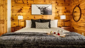 Ett sovrum med träpanel på väggarna, en säng, två sänglampor, en inramad tavla med en tjur på och ett brickbord med jordgubbar och en mugg.