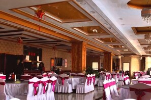 A banquet hall with round tables, chairs with pink sashes, and a stage area. - Wuzhou Hotel (Yongchang)
