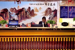 A reception desk with a computer, a plant, and a framed picture of mountains. - Wuzhou Hotel (Yongchang)