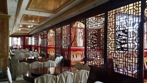A restaurant with round tables and cushioned chairs, a decorative wooden partition, and a red and white color scheme. - Wuzhou Hotel (Yongchang)