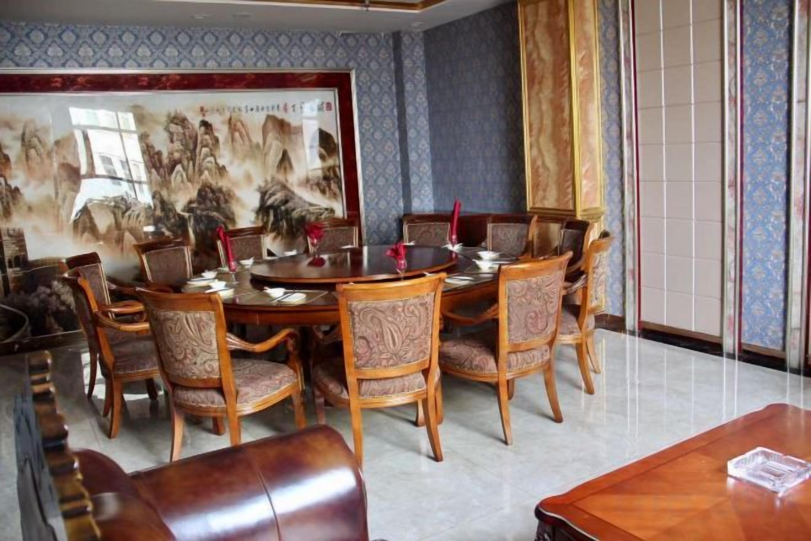 A traditional dining room with a round table and chairs, a large painting on the wall, and a sliding door.