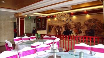 A hotel lobby with round tables, chairs with pink sashes, a red railing, and a mural with Chinese characters.
