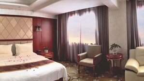 A hotel room with a bed, two chairs, a small table, a potted plant, and a window with curtains. - Wuzhou Hotel (Yongchang)