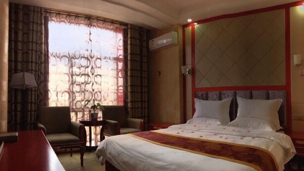 A hotel room with a large bed, two armchairs, a small table, and a desk. - Wuzhou Hotel (Yongchang)