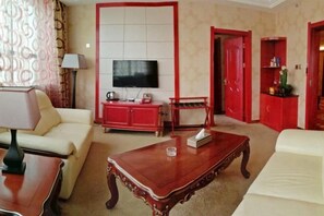 A hotel room with a television, a sofa, a coffee table, a red cabinet, and a red door. - Wuzhou Hotel (Yongchang)