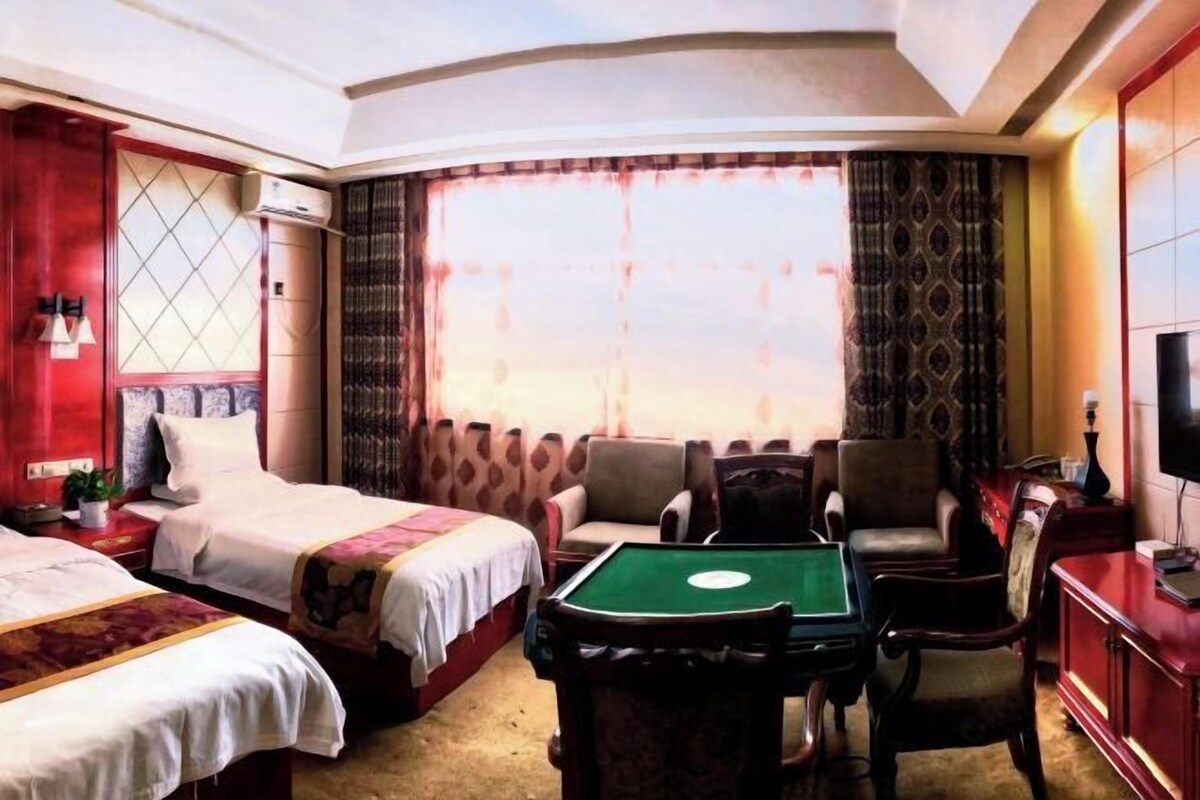 A hotel room with two beds, a pool table, a TV, and a large window with curtains.