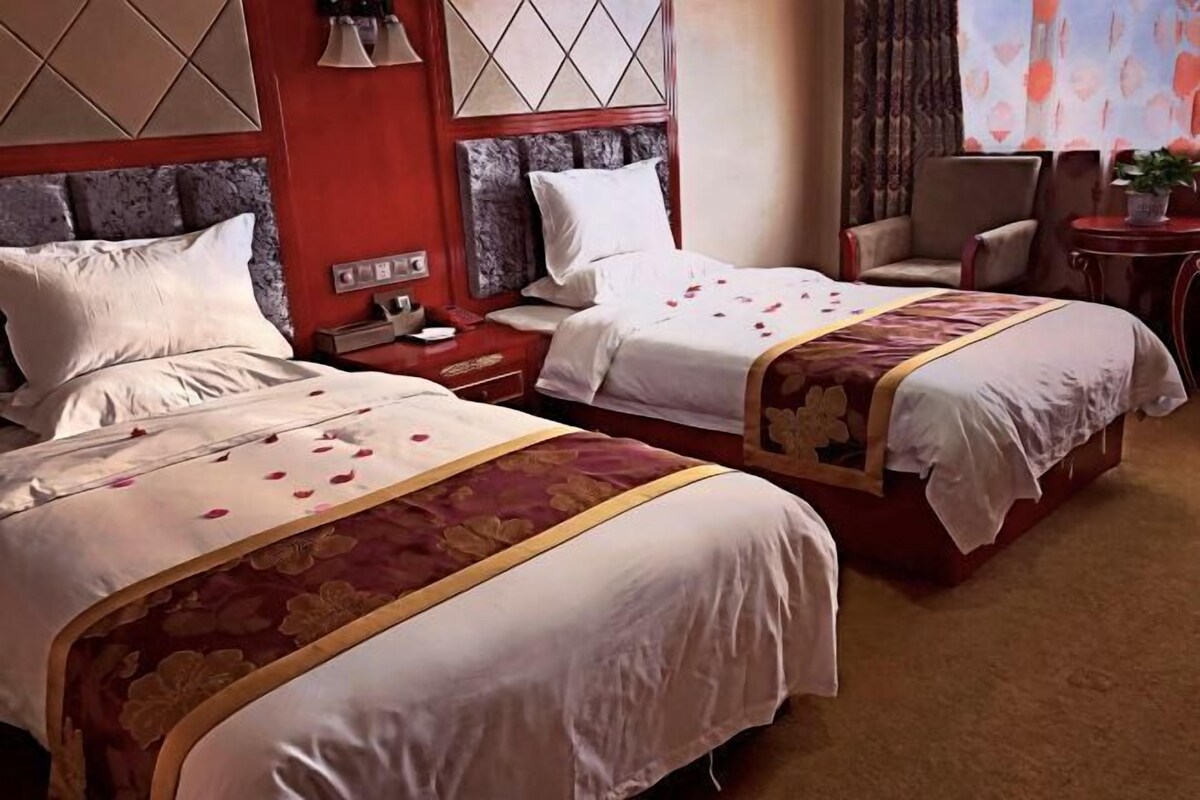 A hotel room with two beds, a nightstand, a chair, and a small table with a plant.