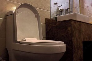 A toilet with a closed lid in a bathroom with tiled walls and a marble accent wall. - Wuzhou Hotel (Yongchang)