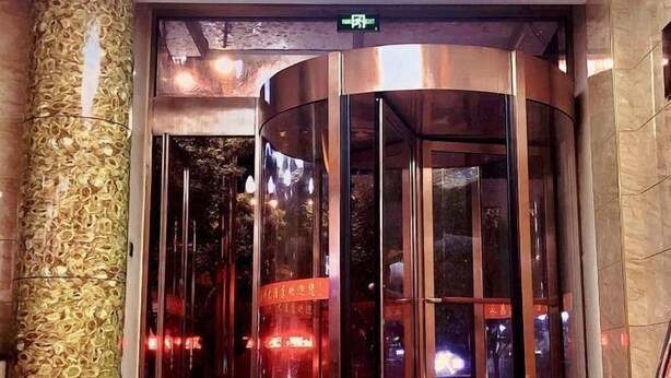 A modern elevator with glass panels and metallic accents, surrounded by a textured wall and a sign with Chinese characters. - Wuzhou Hotel (Yongchang)